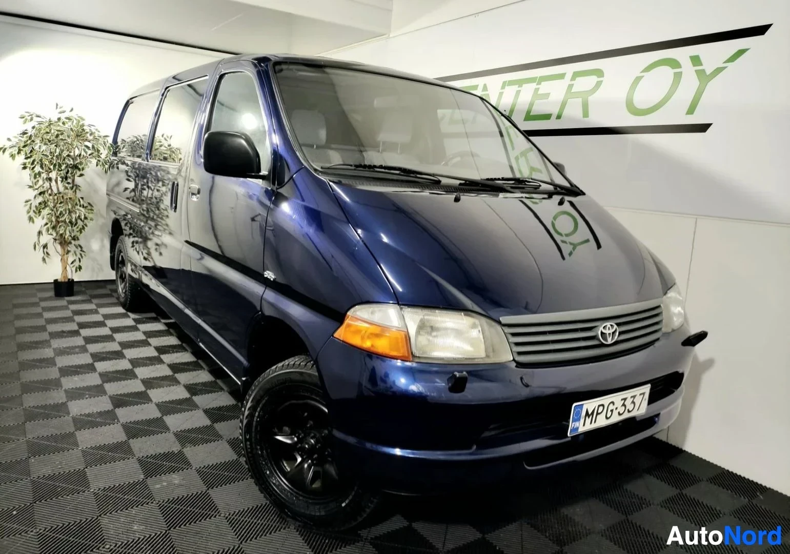 Etuviisto, nokka oikealle: Sininen pakettiauto etukulmasta oikealta, rekisteritunnus.