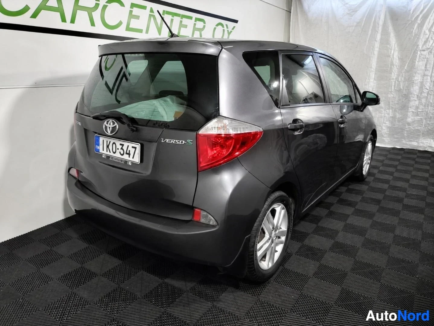 Takaviisto: Tummanharmaa Toyota Verso-S takaviistoon kuvattuna, takavalo ja Verso-S-teksti näkyvissä.