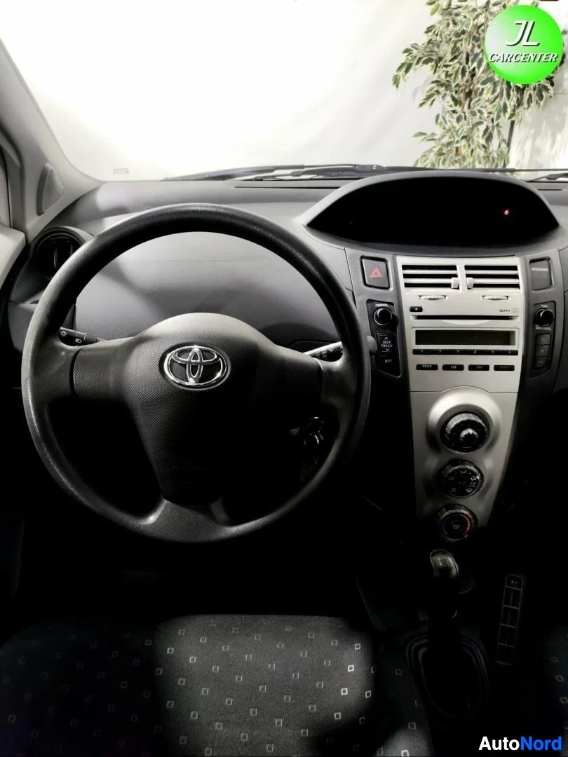 Muu: Pystysuora kuva ohjaamosta: Toyota-ohjauspyörä ja keskikonsoli ilmastointiaukeilla ja radiolla.