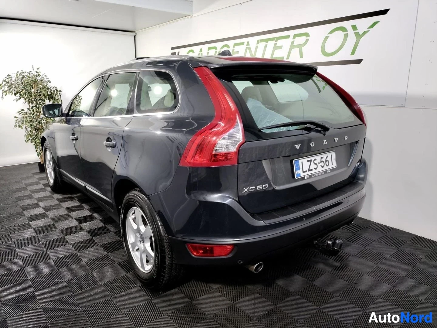 Takaviisto: Volvo XC60 -farmarin takakulmanäkymä: tummanharmaa korivaunu, rekisterikilpi ja vetokoukku näkyvät sisätiloissa otetussa kuvassa.