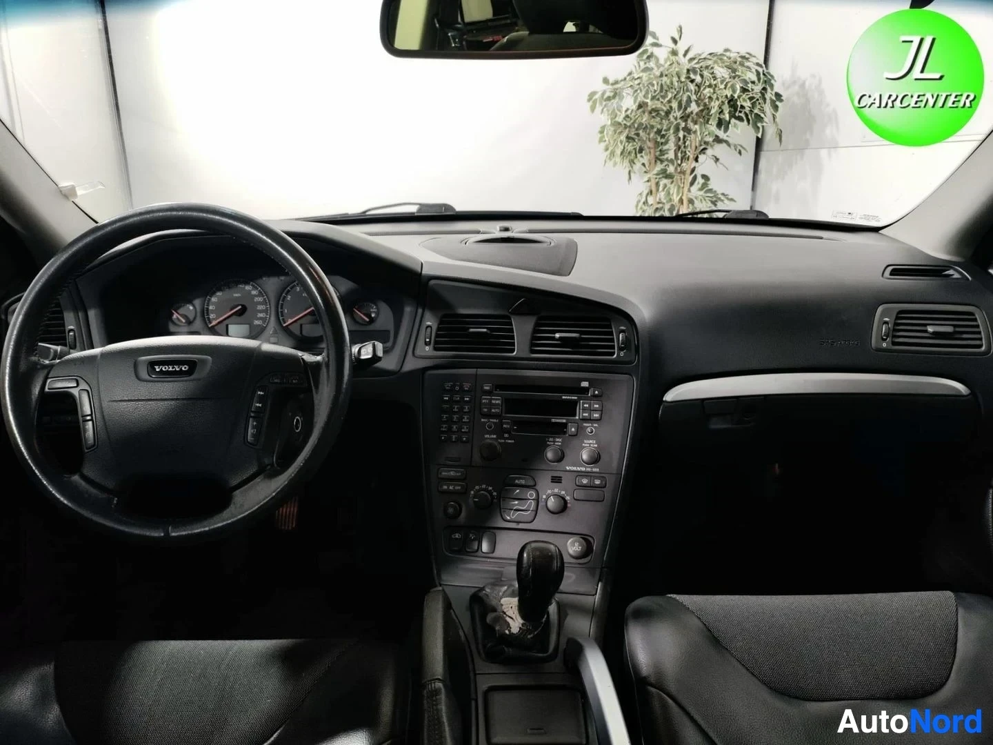 Ohjaamo: Volvo-ohjaamo ylhäältä: ratissa VOLVO-logo, automaattivaihteen valitsin ja keskiö paneelineineen
