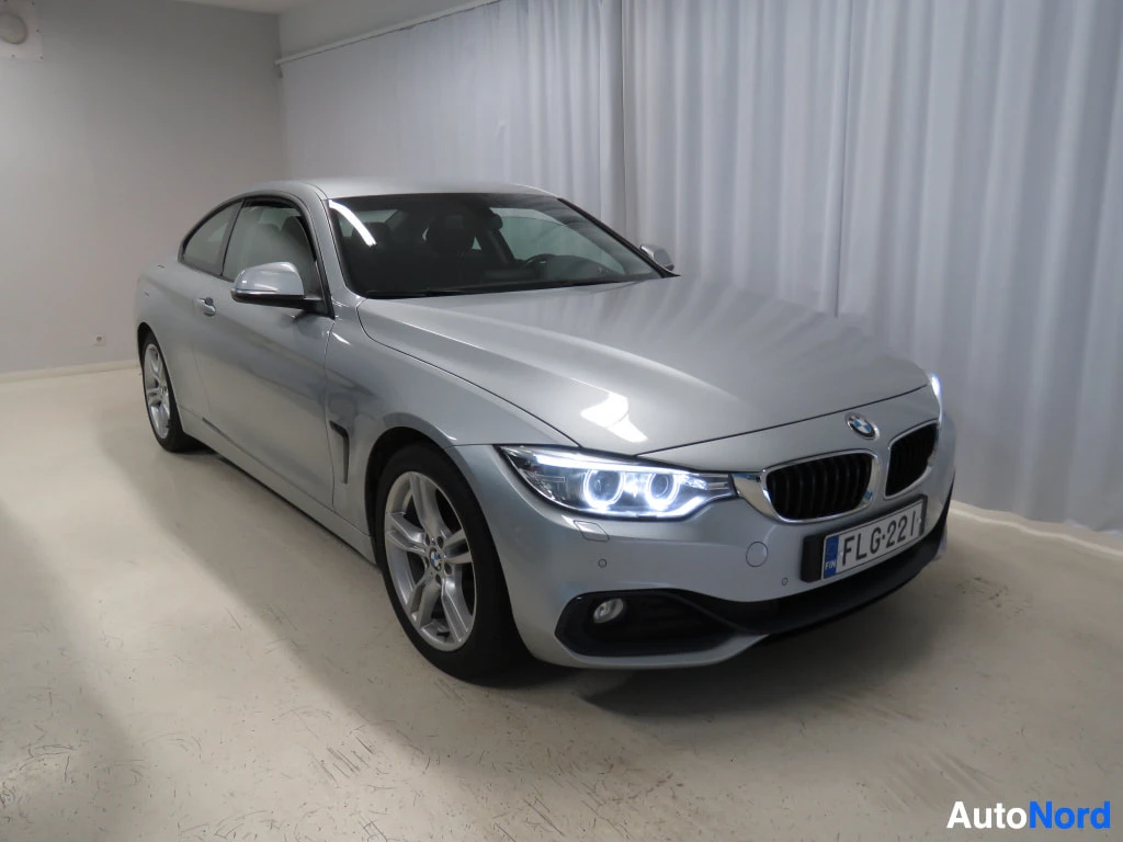 Etuviisto, nokka oikealle: Hopeanharmaa BMW-coupé kulmaetunäkymässä sisätiloissa, valoisa kuva.
