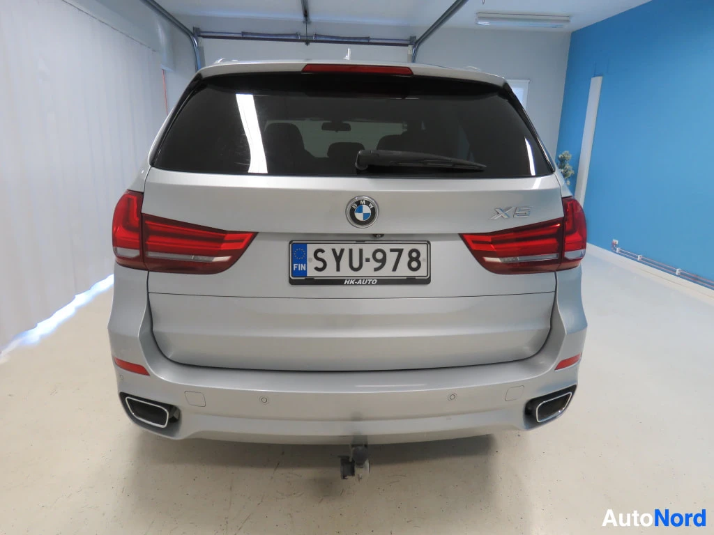 Takaa: BMW:n takapää halleissa: suorakulmaiset takavalot, X5-merkintä, rekisterikilpi ja hinauskoulu takapuskurin alla.