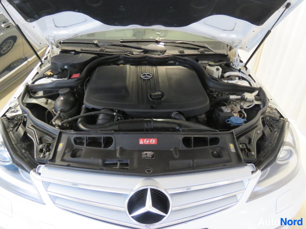 Edestä: Auki nostetulla konepellillä varustetun valkoisen Mercedes-Benzin moottoritila, jossa näkyy Mercedes-tähdellä varustettu moottorin kansi.