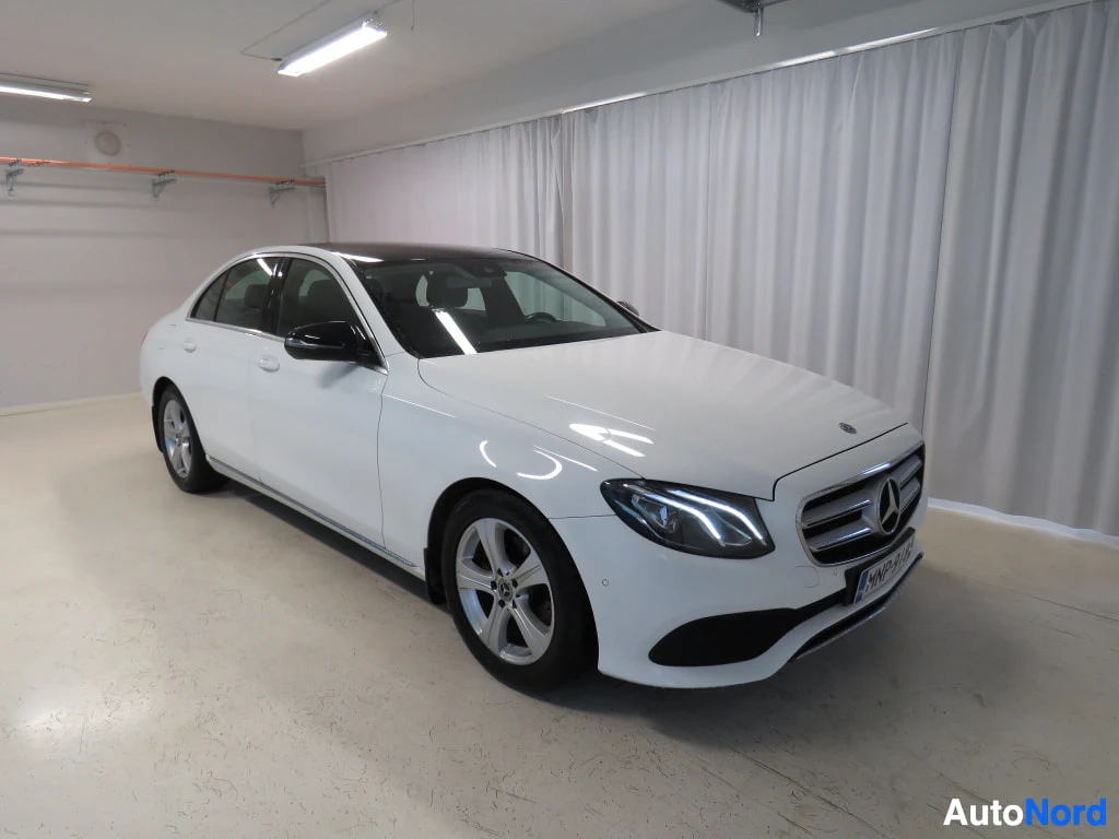 Etuviisto, nokka oikealle: Mercedes-Benz E-sarjan sedan etuviistosta oikealta, valkoinen kori, valkoista verhoa taustalla.