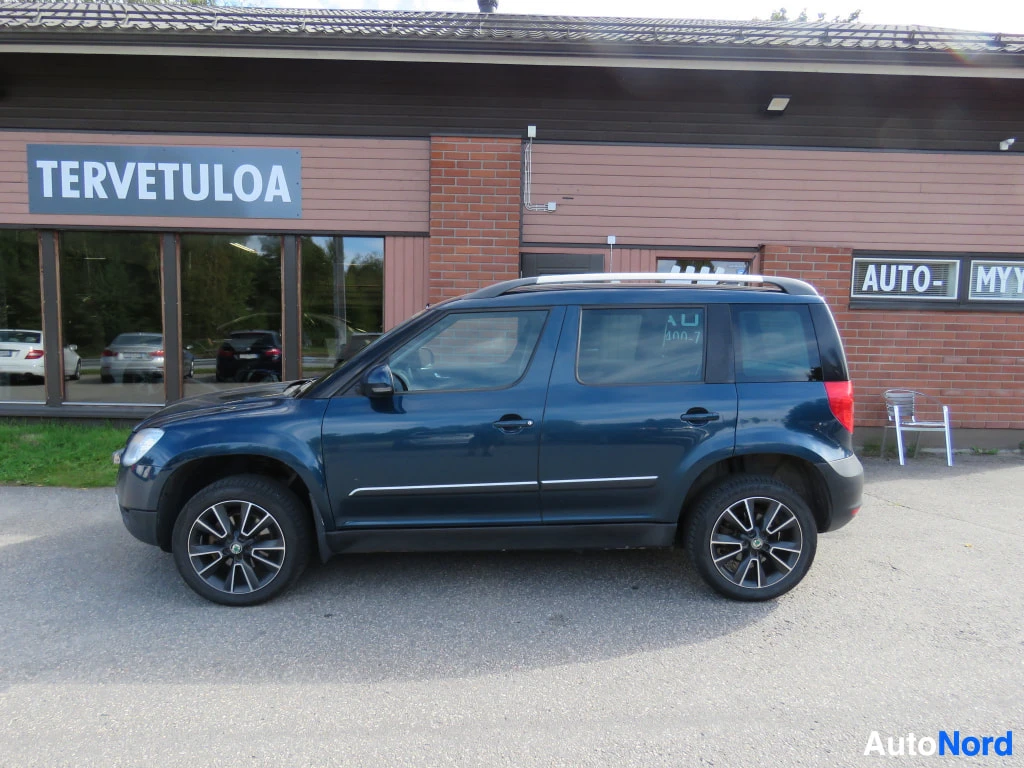 Etuviisto, nokka vasemmalle: Sininen Skoda Yeti sivulta oikealta, kattokaiteet ja viisiovisuutinen näkyvät.