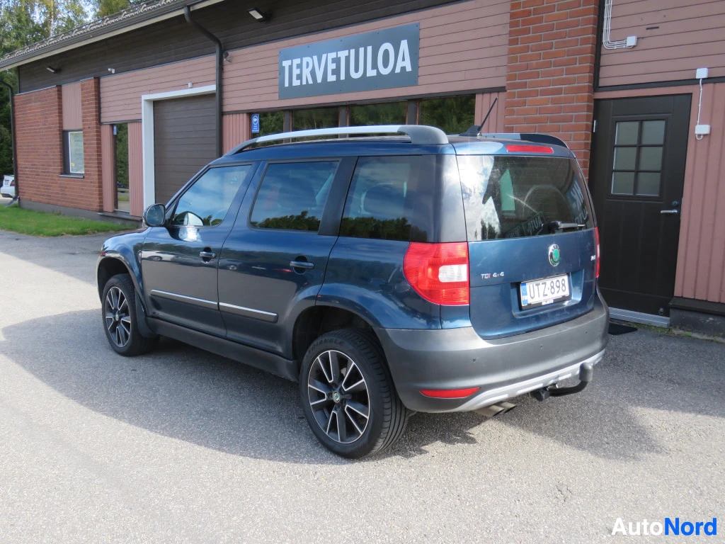 Takaviisto: Sininen Skoda Yeti takakulmasta vasemmalta, rekisterikilpi ja kattokaiteet näkyvät.
