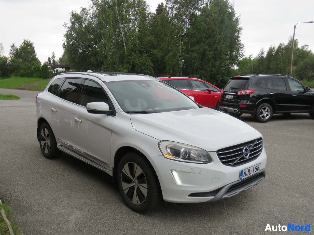 Etuviisto, nokka oikealle: Valkoinen Volvo XC60 farmari kolmivartalo- ja etunäkymässä parkkipaikalla, etupuskurissa rekisterikilpi.