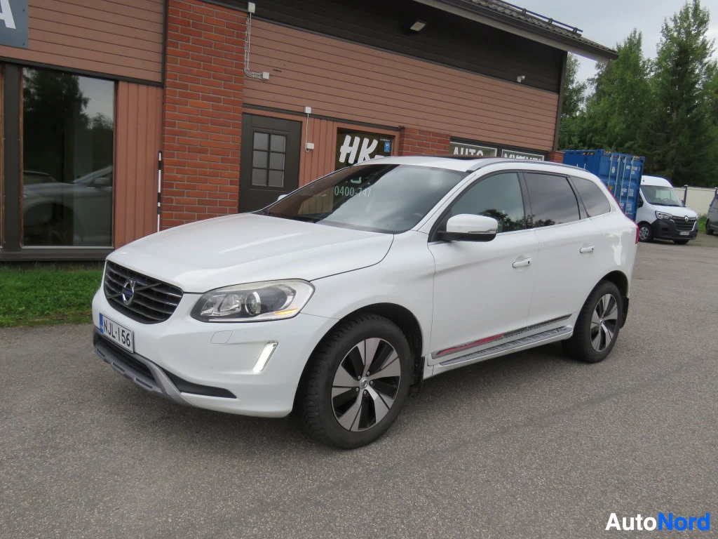 Etuviisto, nokka vasemmalle: Valkoinen Volvo XC60 edestä vasemmalta kolmannelta katsottuna rakennuksen edustalla.