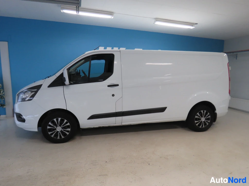 Sivulta: Valkoisen Ford Transit Custom -pakettiauton kylki vasemmalta kuvattuna sinistä taustaa vasten.
