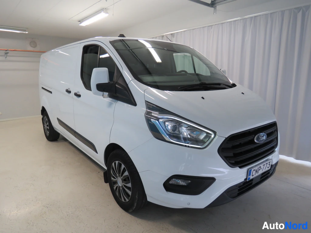Etuviisto, nokka oikealle: Valkoinen Ford Transit Custom -pakettiauto etukulmasta oikealta rekisterillä.