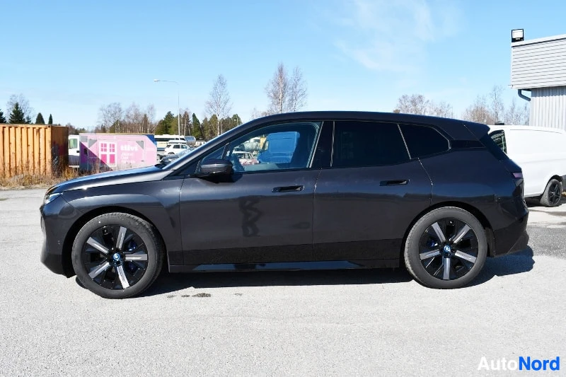 Sivulta: Sivukuva tummanharmaasta BMW iX -maasturista, molemmat sivut ja mustat vanteet näkyvissä.
