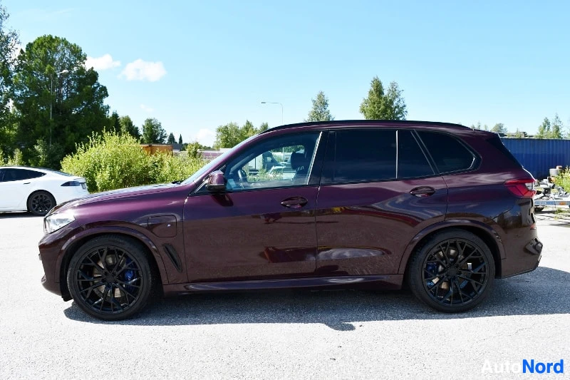 Sivulta: Sivulta kuvattu tummanpunainen BMW X5 -henkilöauto, mustat vanteet.
