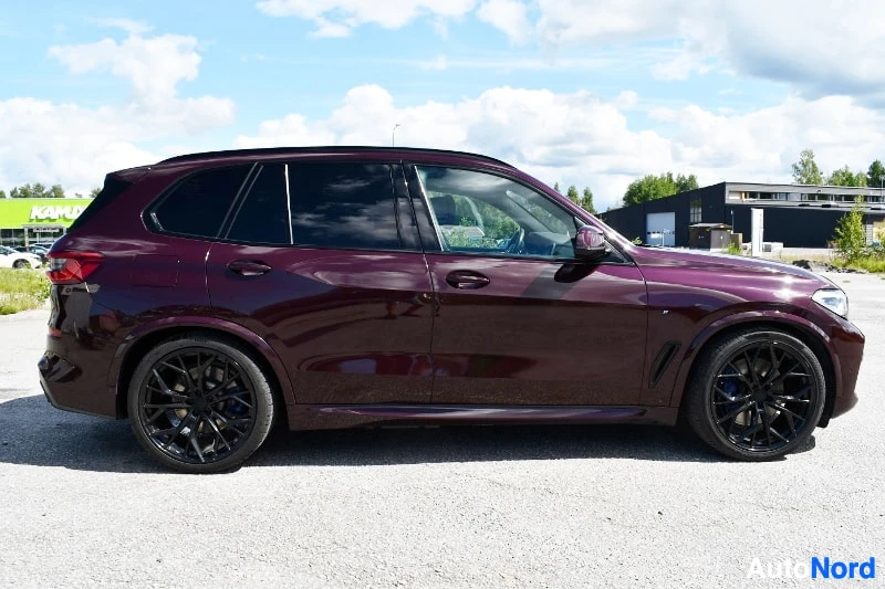 Sivulta: Tummanpunainen BMW X5 -maasturi sivulta kuvattuna mustilla vanteilla.