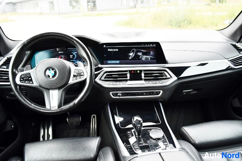 Ohjaamo: Ohjaamo näkyvä BMW:n ratin ja keskinäytön kanssa; kojelauta, vaihtajanopea ja keskikonsoli näkyvät.