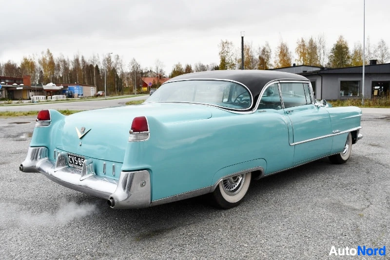 Takaviisto: Vaaleansininen Cadillac Coupe Deville takaa-osittain sivulta kuvattuna, tumma katto ja kromipuskurit