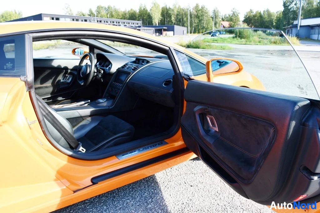 Ohjaamo: Kuljettajan puolen ovi auki, sisätila ja ovinelä näkyvissä oranssin auton sisällä.