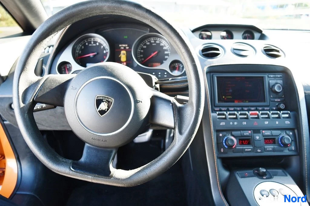 Ohjaamo: Ratin ja kojetaulun lähikuva, Lamborghini-logolla varustettu ohjauspyörä ja mittaristo.