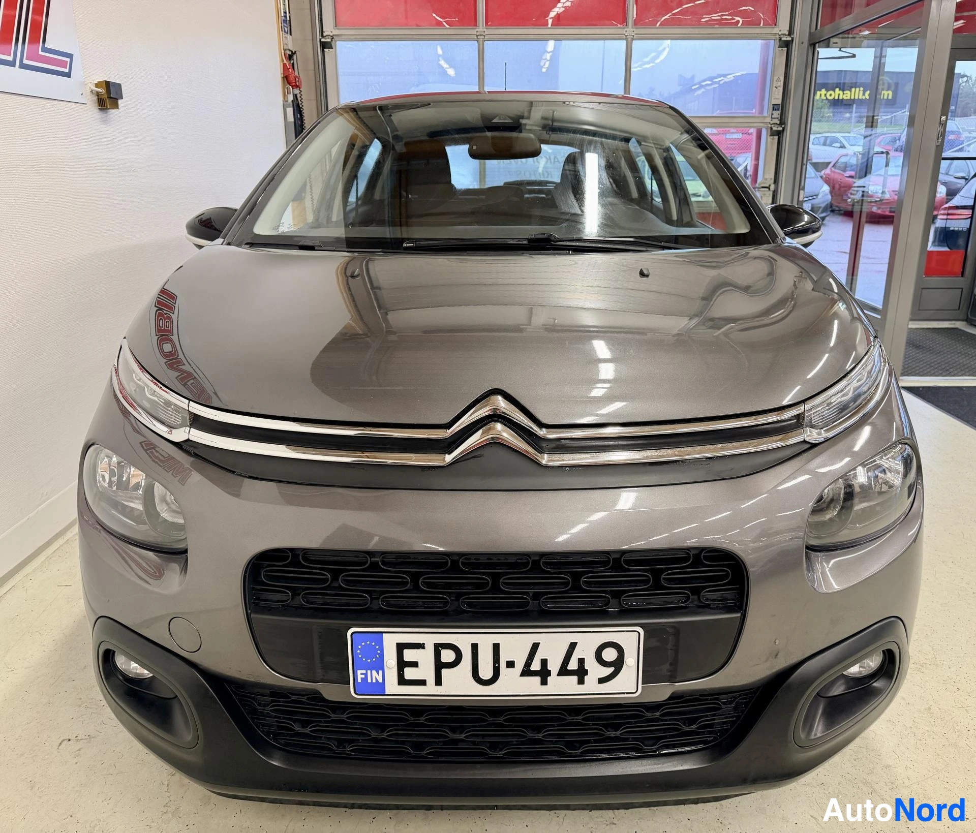 Edestä: Harmaan Citroën C3:n keulakuva; näkyvät kromilista etusäleikössä, sumuvalot ja rekisteritunnus.