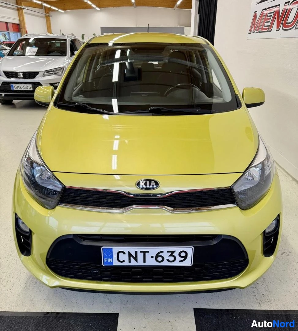Edestä: Keltaisen Kia Picanon etuosa suoraan edestä, Kia-merkki ja rekisteritunnus näkyvissä.