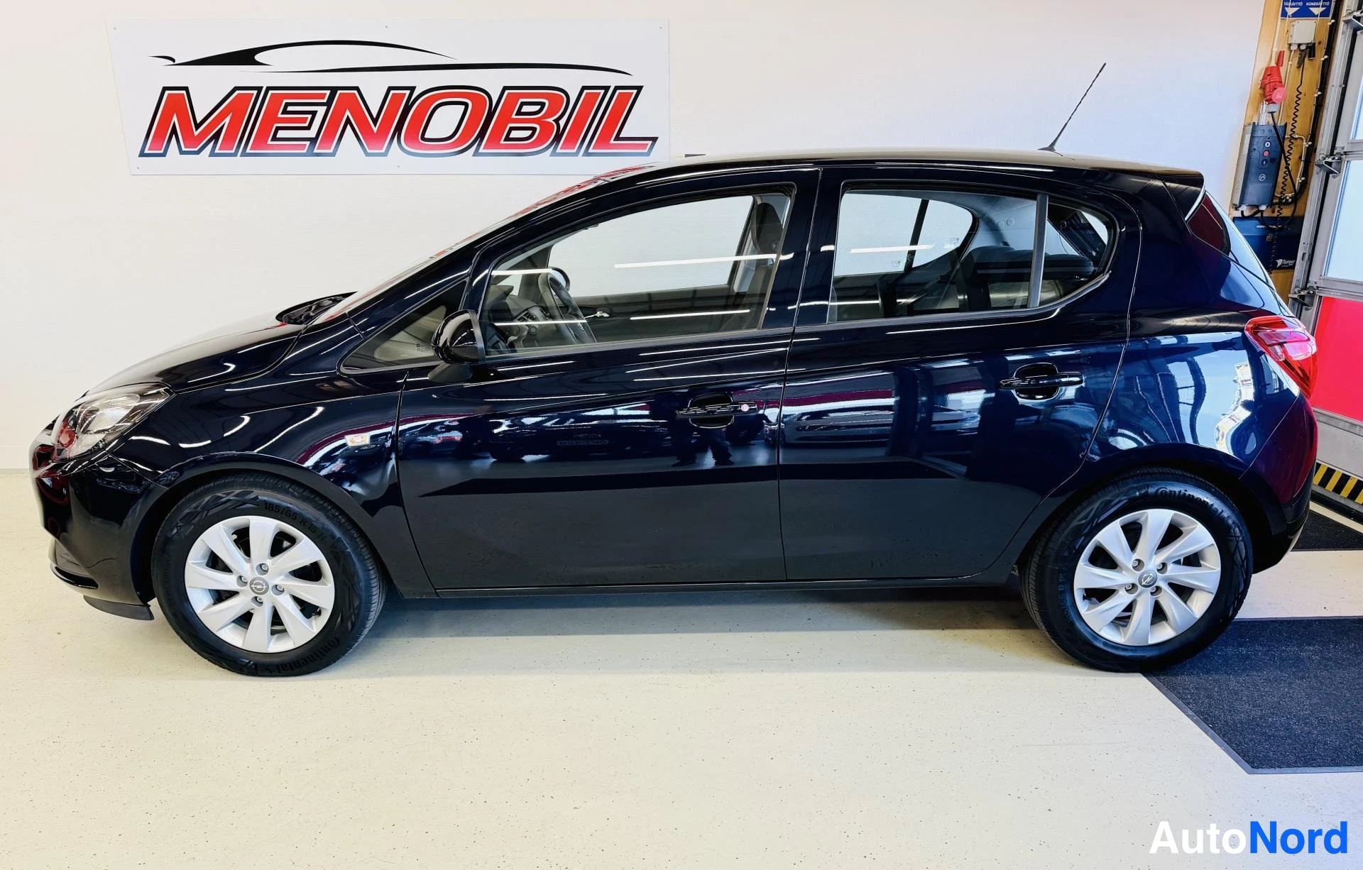 Sivulta: Mustan Opel Corsa -henkilöauton sivukuva oikealta puolelta autosalissa.