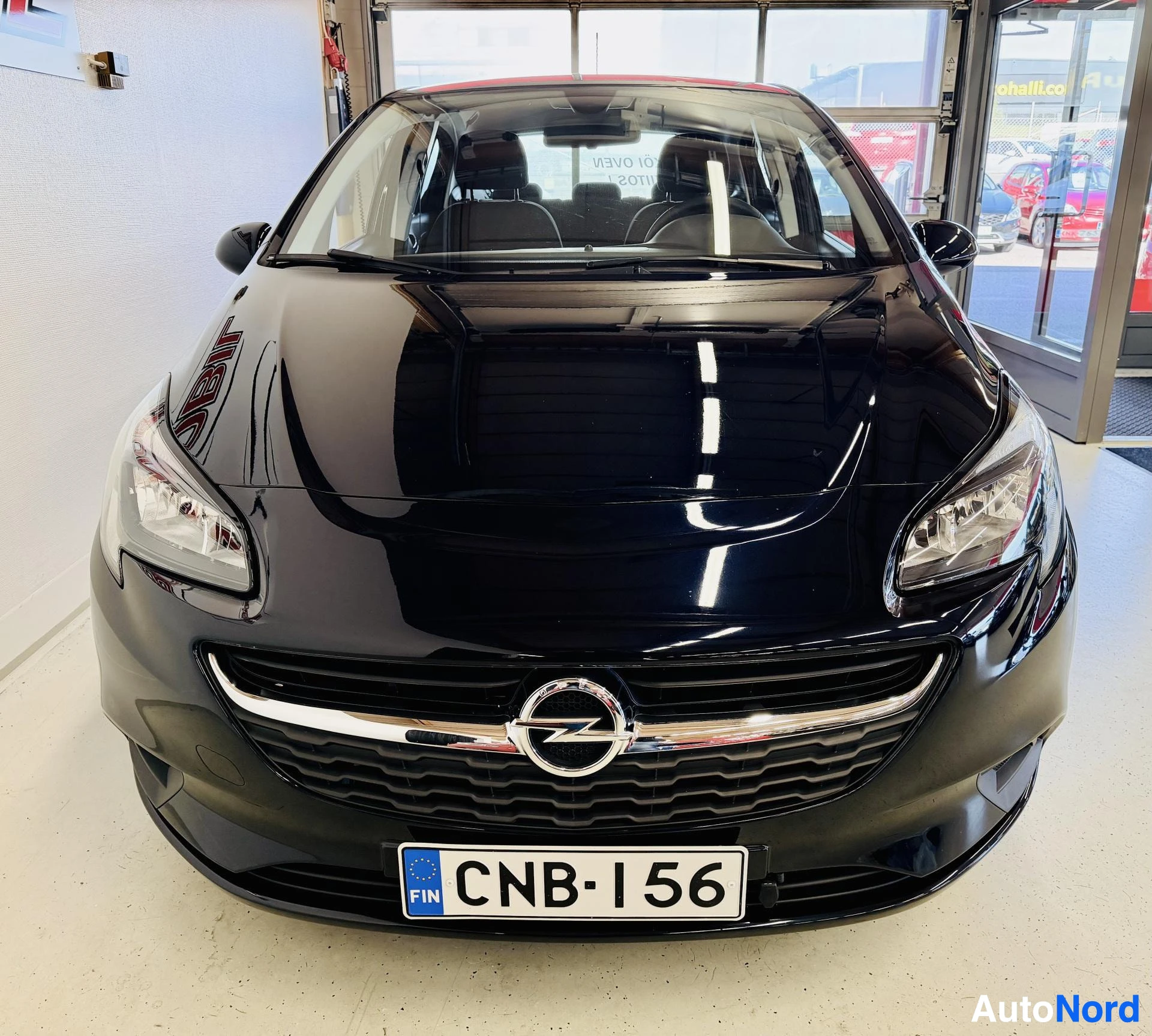 Edestä: Mustan sinertävän tumman Opel Corsa -auton keulakuva; kiiltävä konepelti, Opel-logo etusäleikössä ja rekisterikilpi näkyvät.