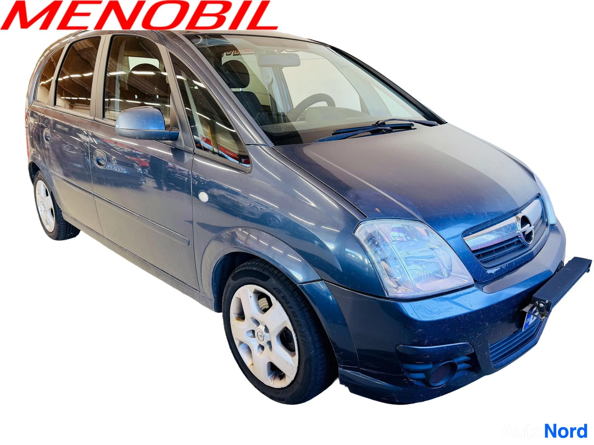 Etuviisto, nokka oikealle: Tummansininen Opel Meriva -henkilöauto etuviistossa, keula osoittava oikealle; etusäleikkö ja ajovalot sekä auton vasemman sivun ovet ja pyörät näkyvät v