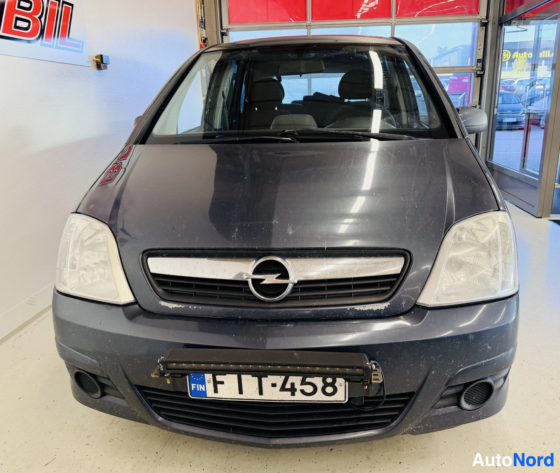 Edestä: Opel Merivan etupää Frontissa: tummanharmaa kori, Opel-merkki keulassa, suomalainen rekisterikilpi ja lisävalo edessä.