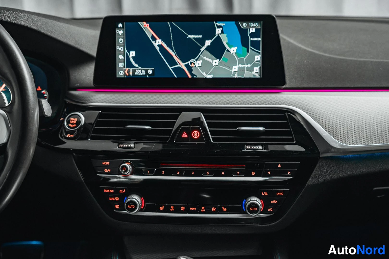 Sivulta: Kojelaudan keskiosan lähikuva: karttaa näyttävä navigointinäyttö, Start/Stop Engine -painike, ilmastointisuuttimet ja AUTO- ja SYNC-merkitsemät säätimet.
