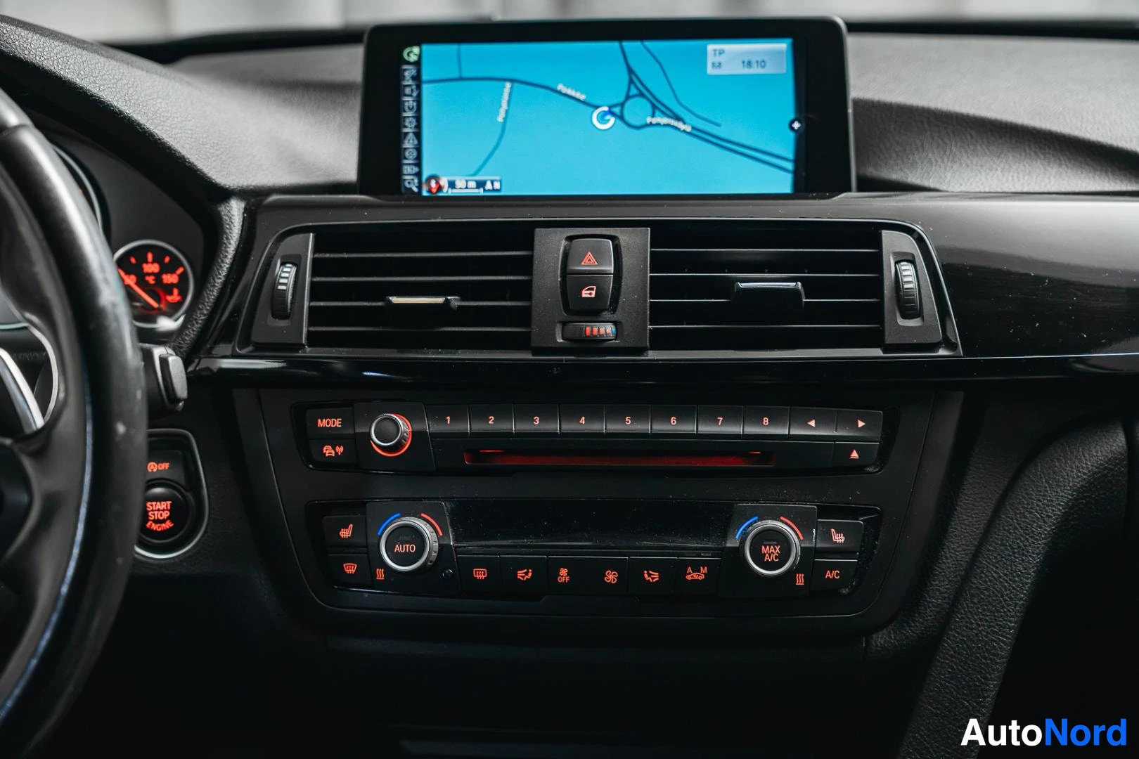 Muu: Keskikonsolin läheiskuva: karttanavigaationäyttö, radiopaneeli ja automaattinen kaksivyöhykeilmastointi (AUTO, MAX DEF), vasemmalla START STOP ENGINE -painike.