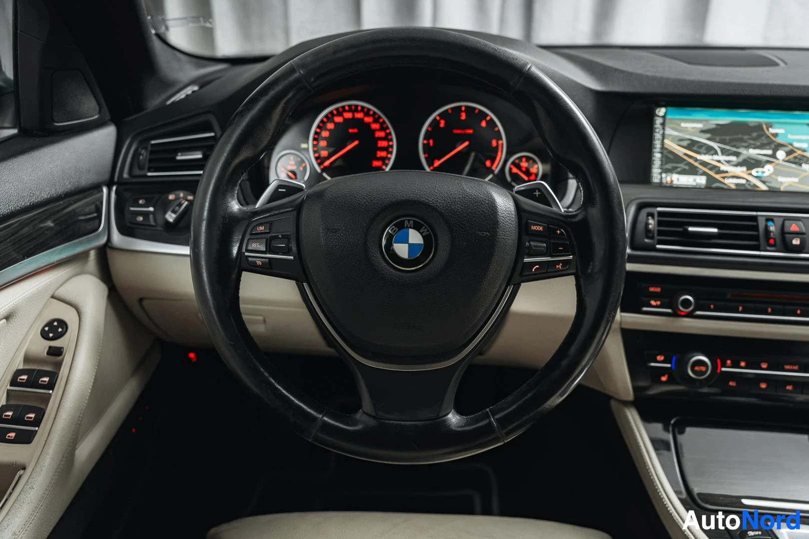 Edestä: BMW-ohjauspyörä ja mittaristo punaisilla taustavaloilla, karttanäyttö oikealla.