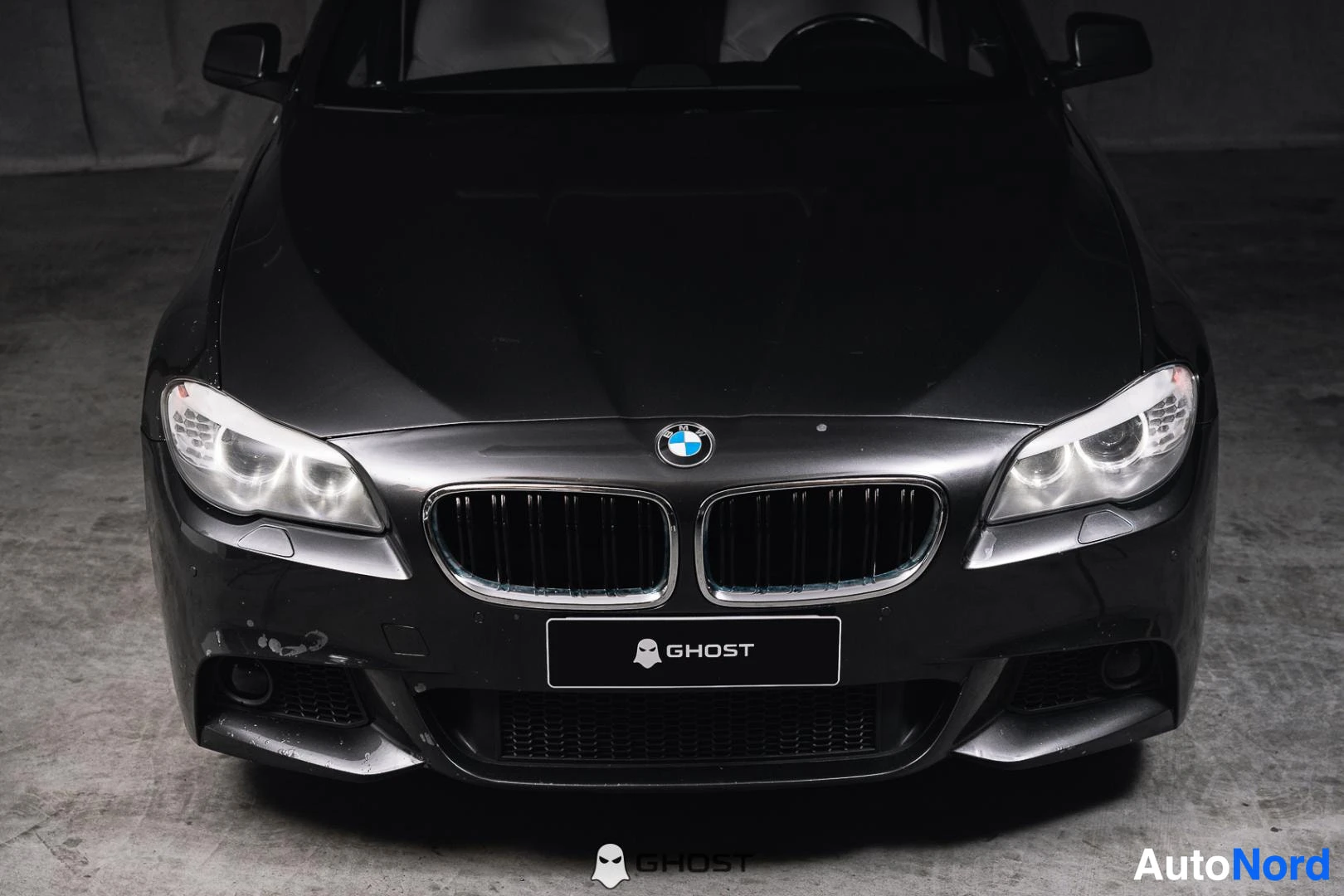 Edestä: Musta BMW:n etuosa lähikuvassa ylhäältä, konepelti, etusäleikkö ja ajovalot näkyvät.