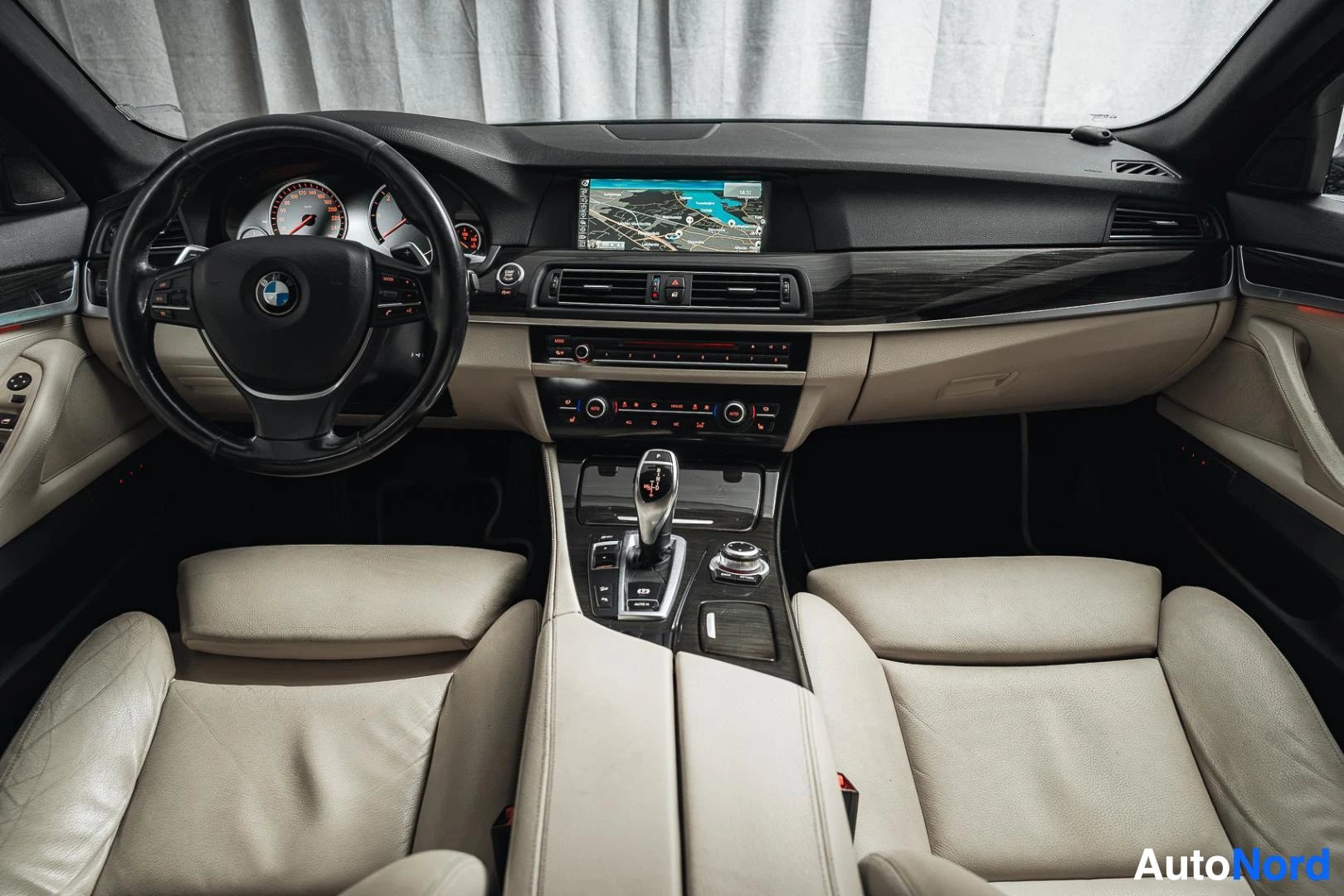 Edestä: Autojen sisätilat: BMW-ohjauspyörä, karttanäyttö, kaksivärinen kojelauta ja beige nahkapenkit.