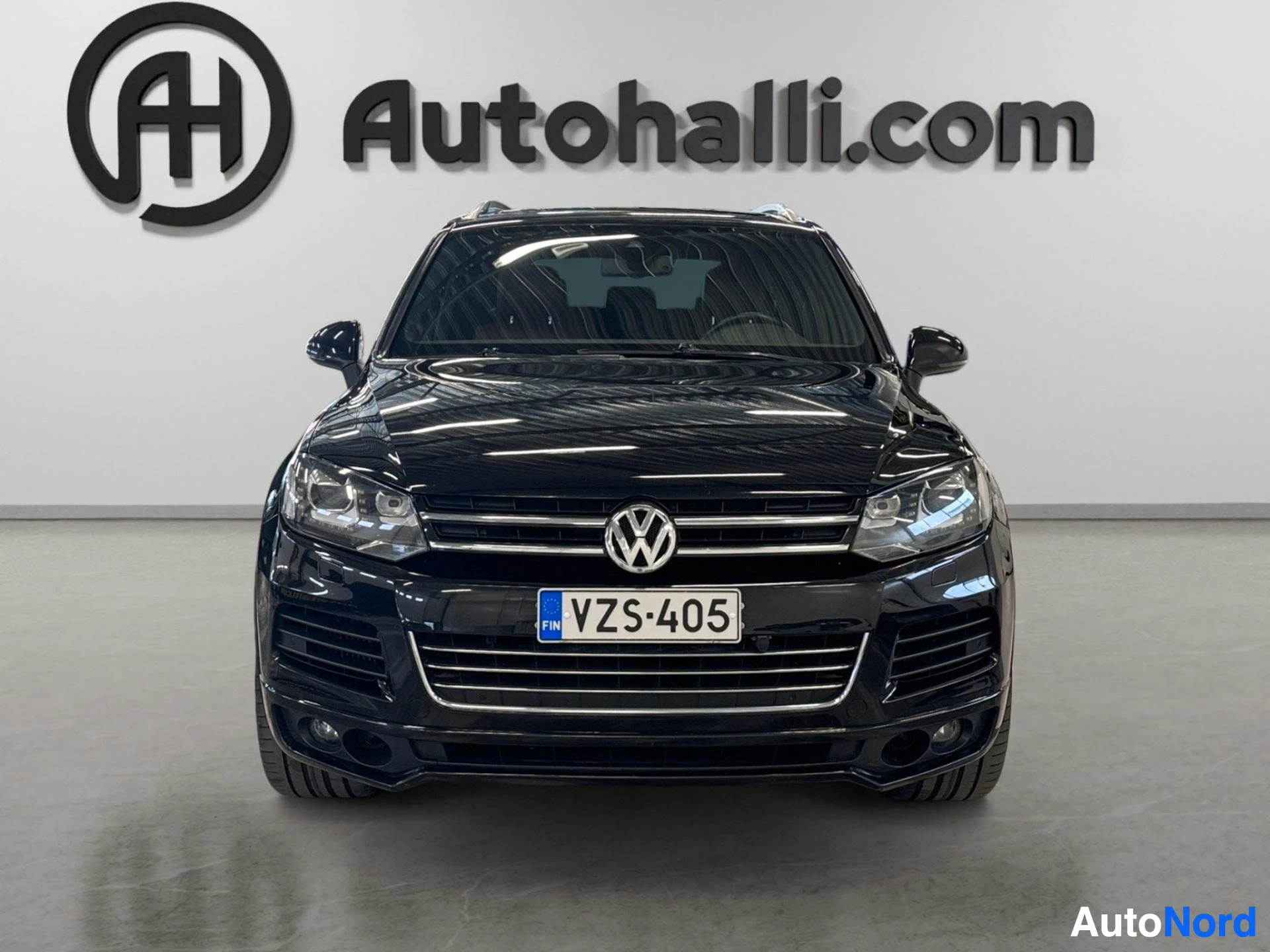 Edestä: Mustan Volkswagenin suora etukuva, VW-merkki ja rekisterikilpi.
