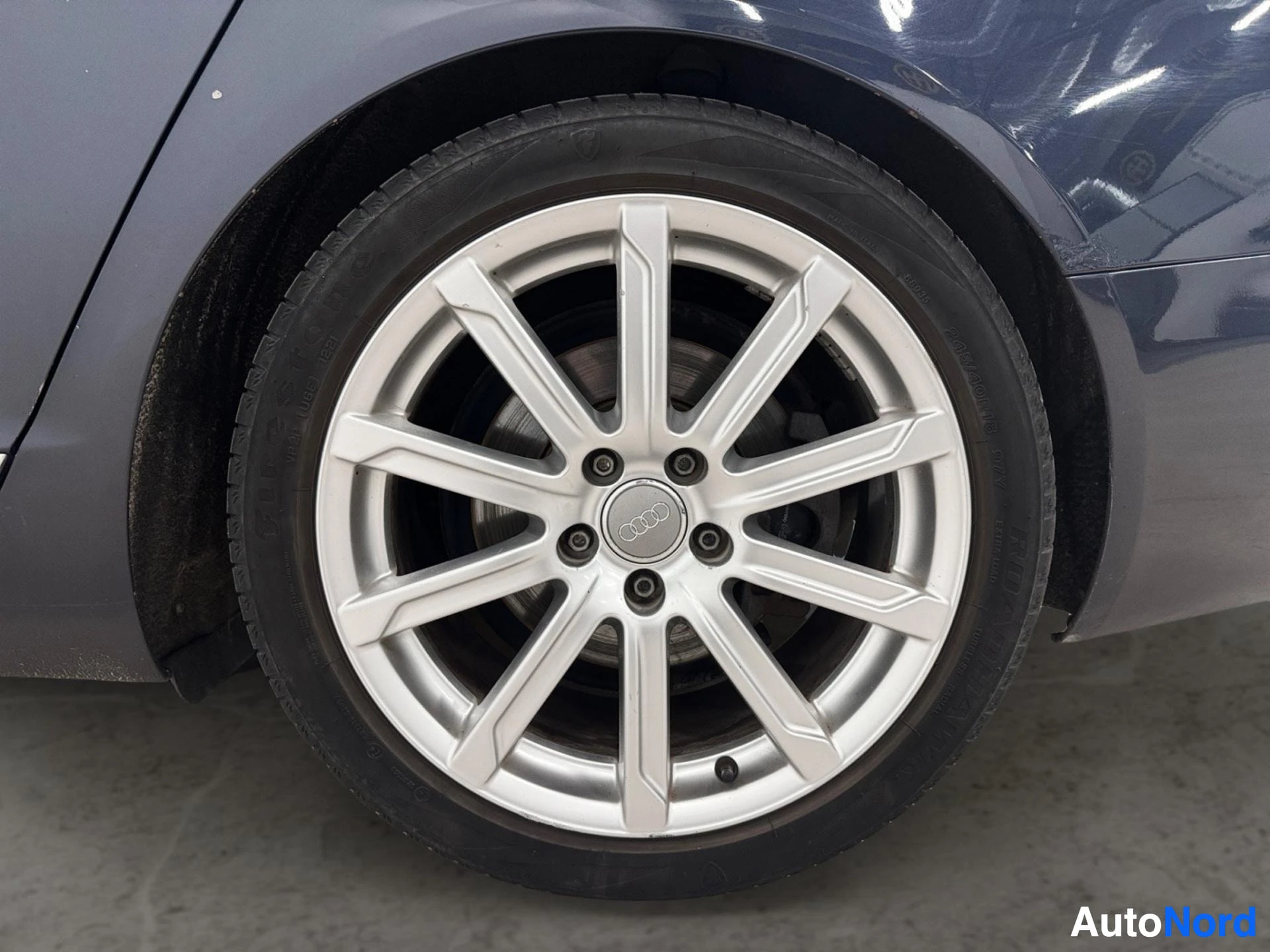 Yksityiskohta: Hopeinen Audi-aluvanne ja kesärengas lähikuvassa.