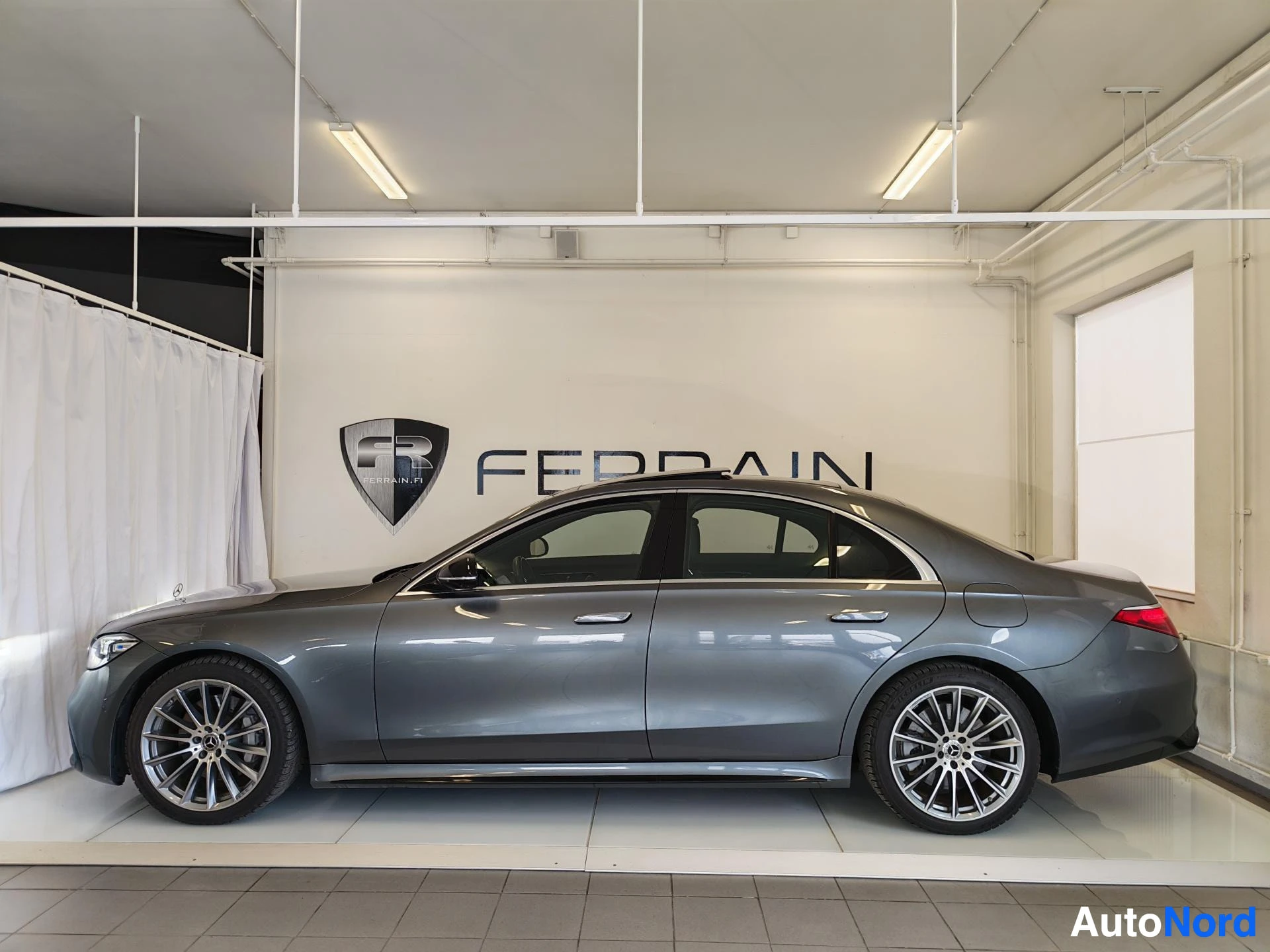 Sivulta: Mercedes-Benz S-luokan sedan sivukuva oikealta, tummanharmaa sedan ja kevytmetallivanteet sisätiloissa.