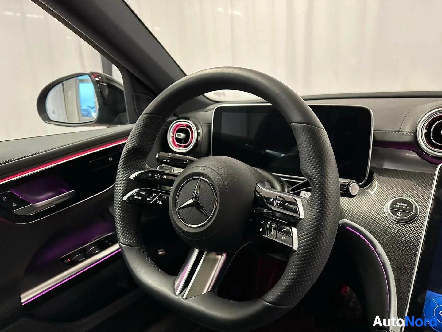 Yksityiskohta: Lähikuva Mercedes-ohjauspyörästä ja kojelaudasta; ENGINE START/STOP -nappi näkyy keskikonsolissa.