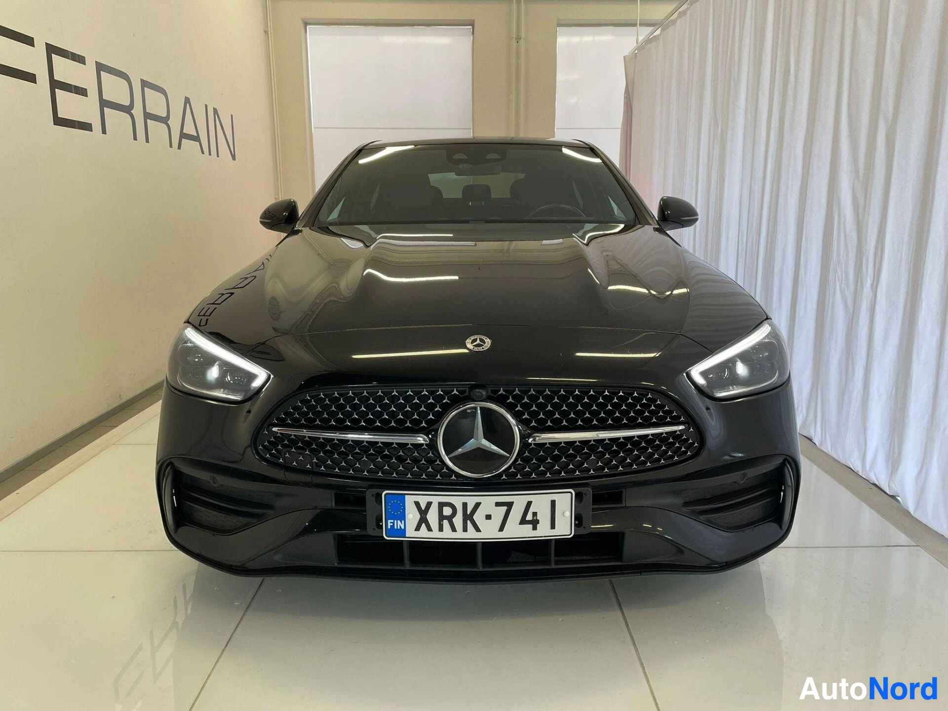 Edestä: Mustan Mercedes-Benzin suora etunäkymä, tähtitunnus konepellissä ja rekisterikilpi.
