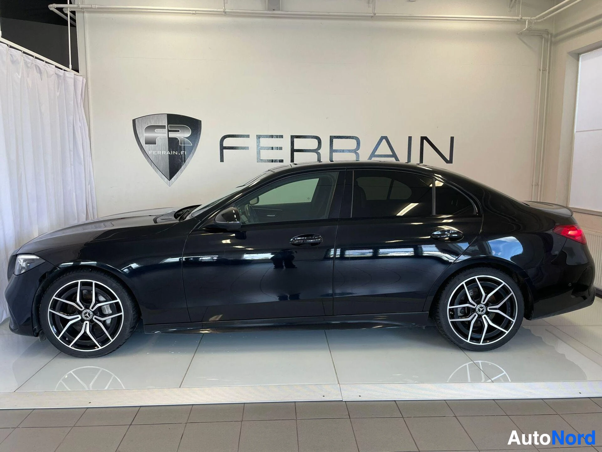 Sivulta: Mustan Mercedes-Benz C -sedanin sivunäkymä showroomin valkoisella lattialla.