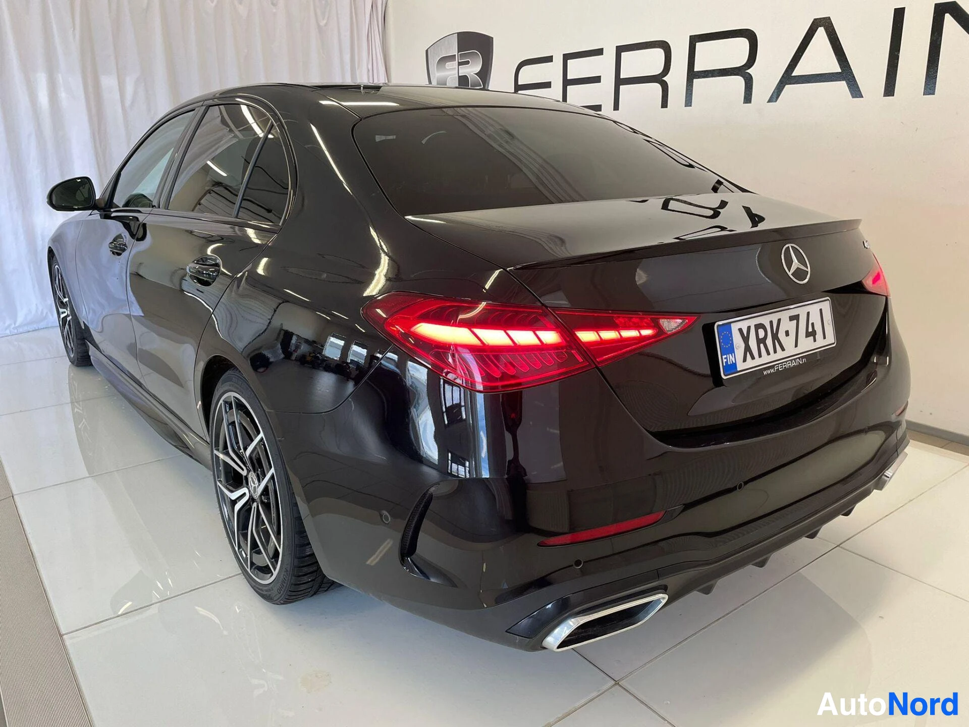 Takaviisto: Musta Mercedes-Benz-sedan takaa kulmasta, rekisterikilpi.