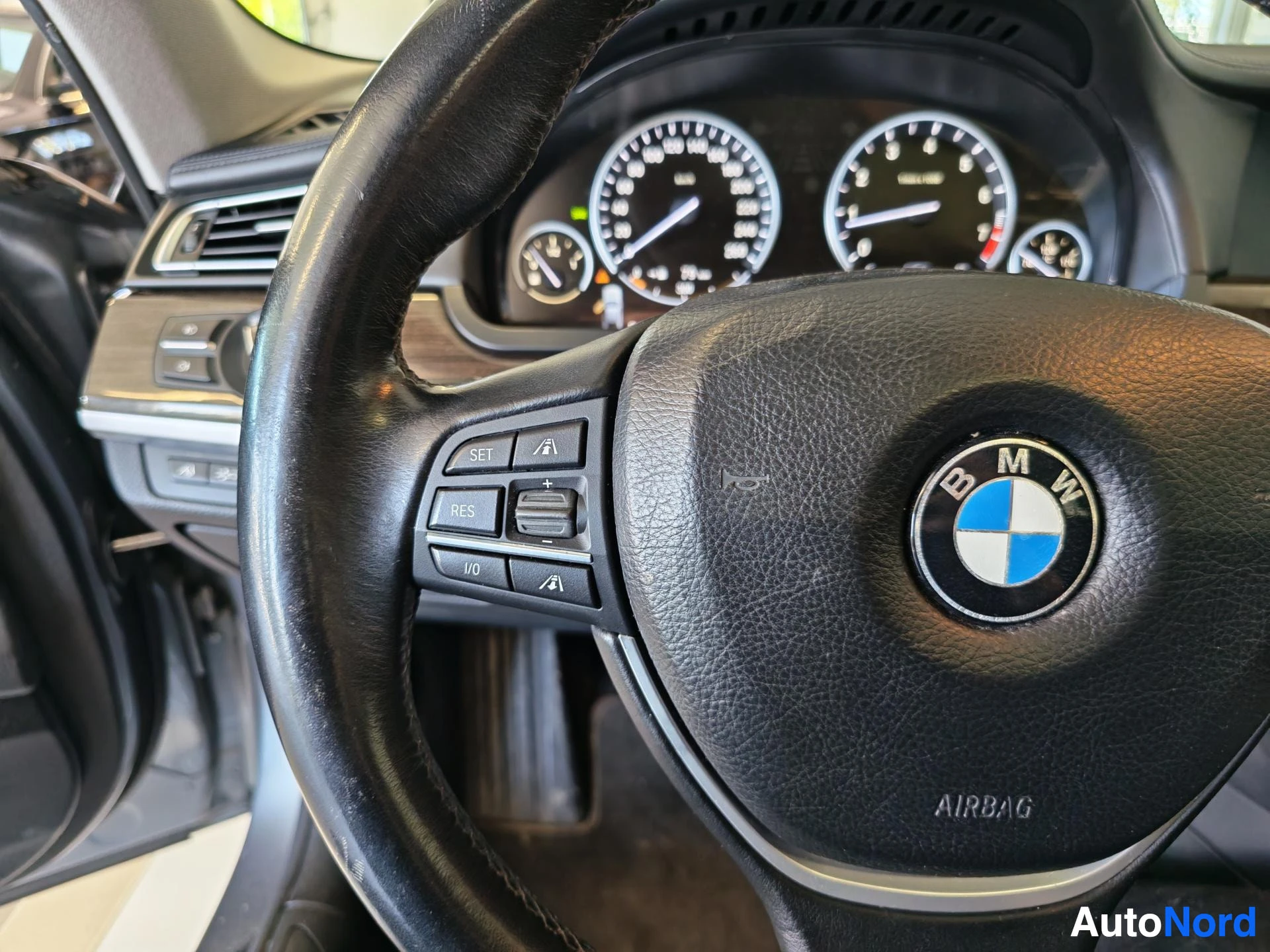 Ohjaamo: BMW-merkillinen ohjauspyörä, vasemman palkin napit SET, RES ja L/O, kojelaudan mittarit taustalla.
