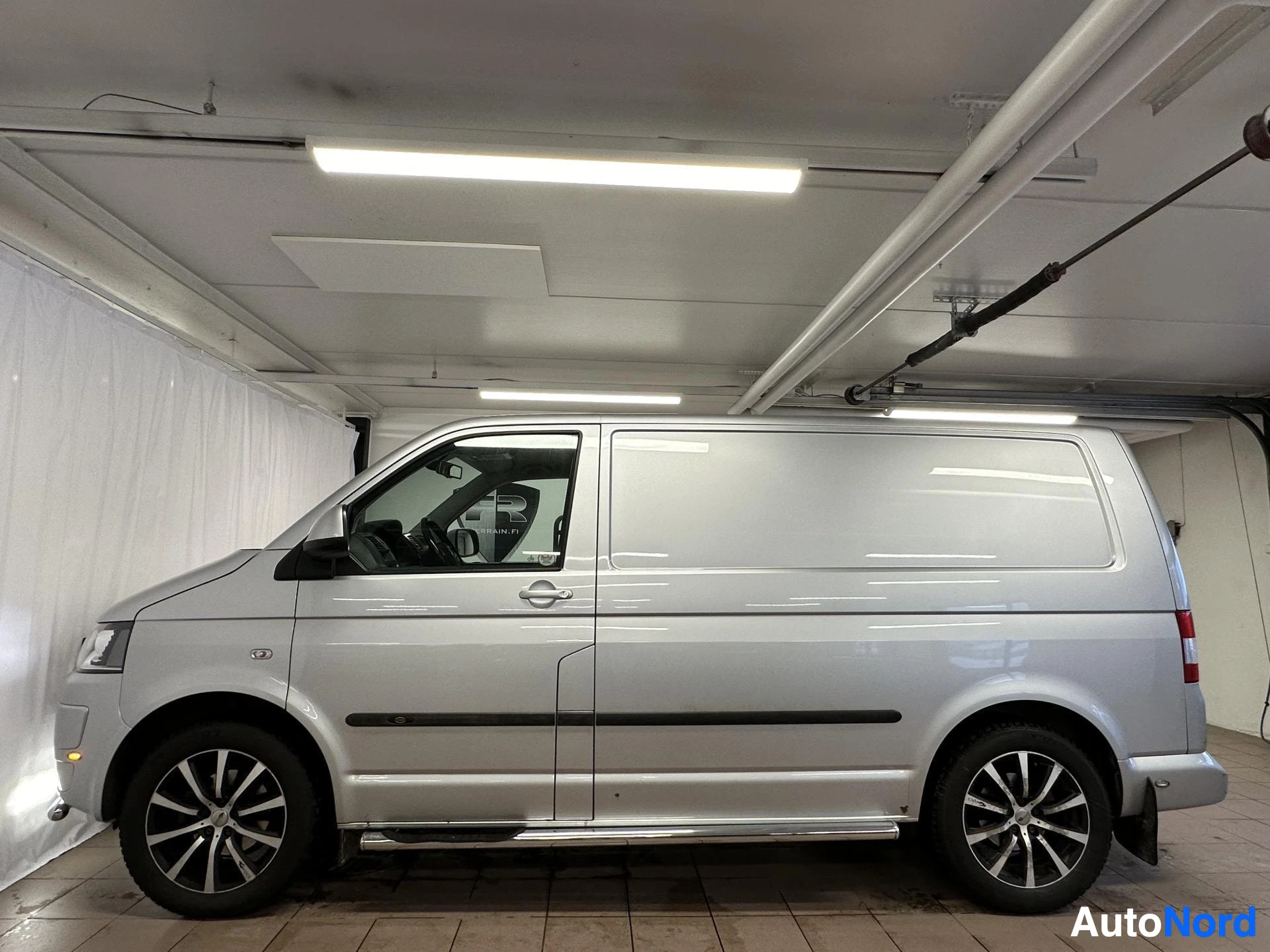Sivulta: Hopeanvärinen Volkswagen Transporter -pakettiauto sivulta kuvattuna autotallissa.