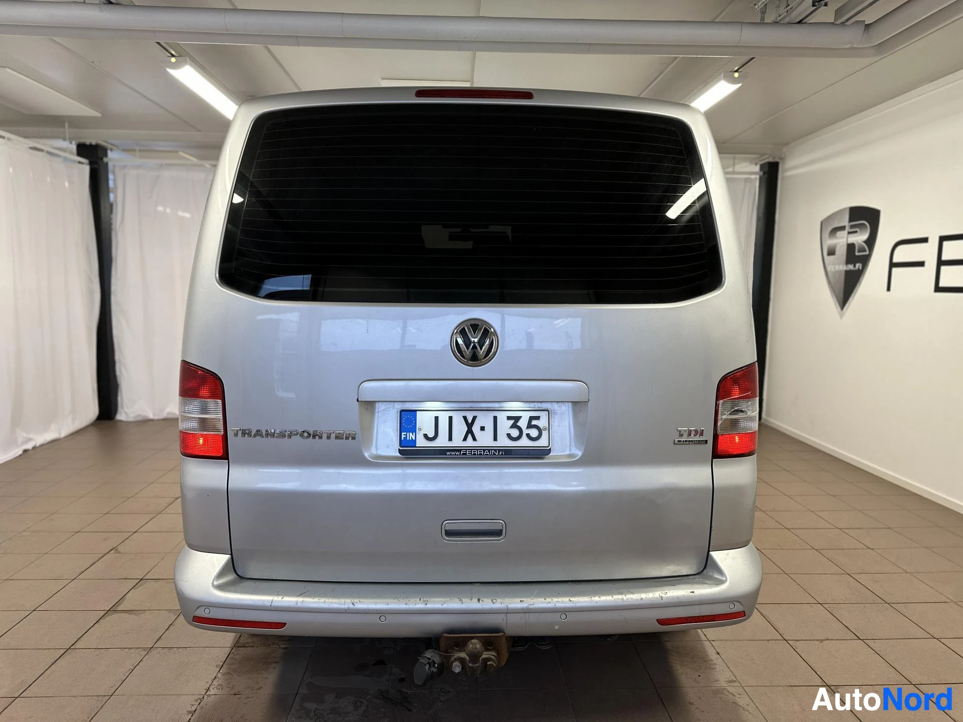 Takaa: Hopeanvärinen Volkswagen Transporter takaa kuvattuna; rekisteritunnus, TDI-merkintä ja vetokoukku näkyvät.