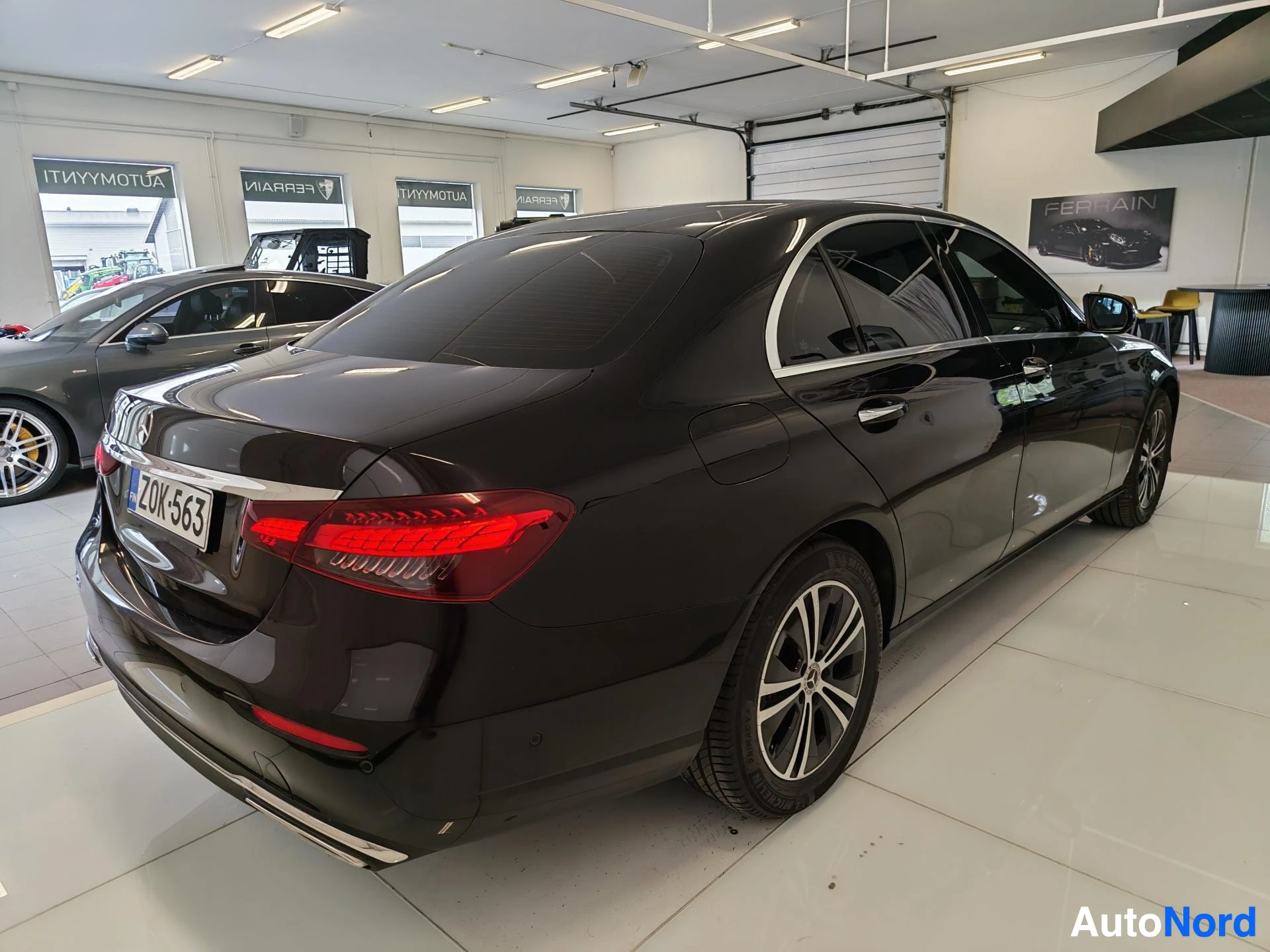 Takaviisto: Mustan Mercedes-Benz E -sedanin takakulma autonhallissa, rekisterikilpi.