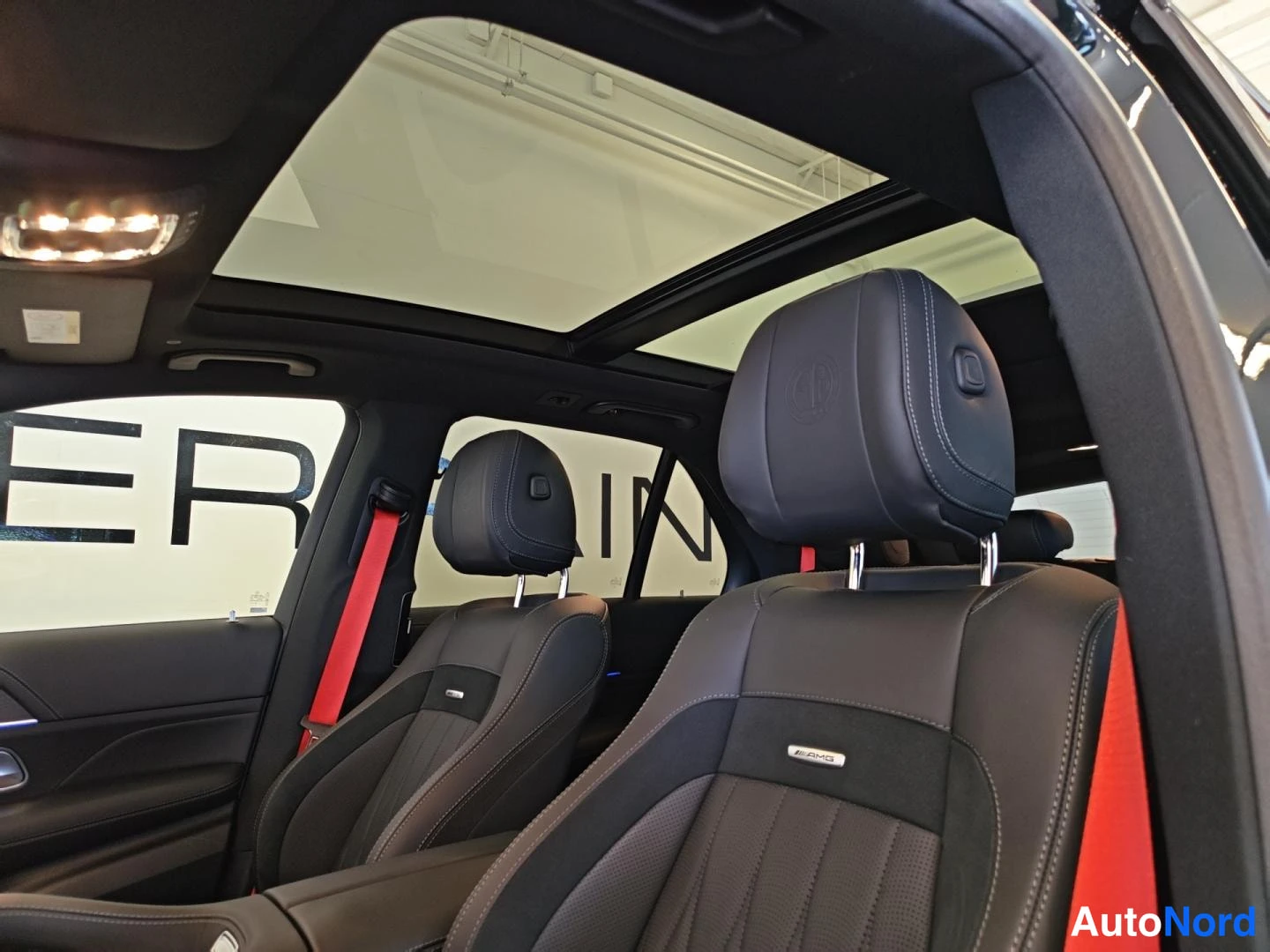 Yksityiskohta: Takapenkin näkymä: kaksi erillistä headrest-tuolia, AMG-merkitty istuin ja punaiset turvavyöt panoramakaton alla.