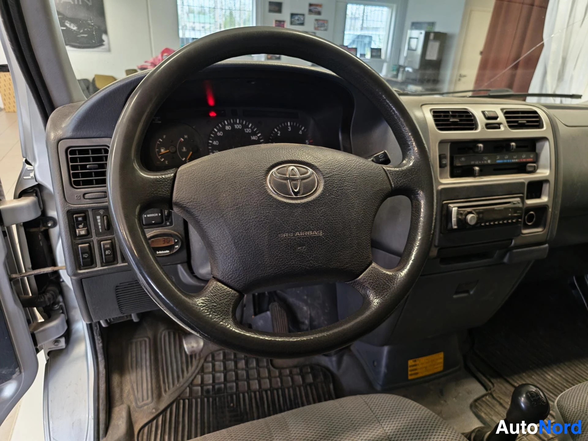 Edestä: Ohjauspyörä ja mittaristo lähikuvassa, Toyota-merkki ja SRS Airbag -teksti näkyvissä.