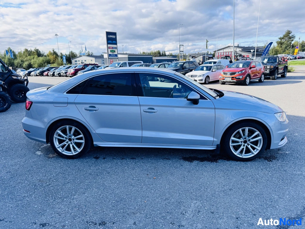 Sivulta: Vaalean hopeanharmaa Audi A3 -sedan sivulta kuvattuna autopaikalla, neljä ovea ja viisisakaraiset alumiinivanteet.