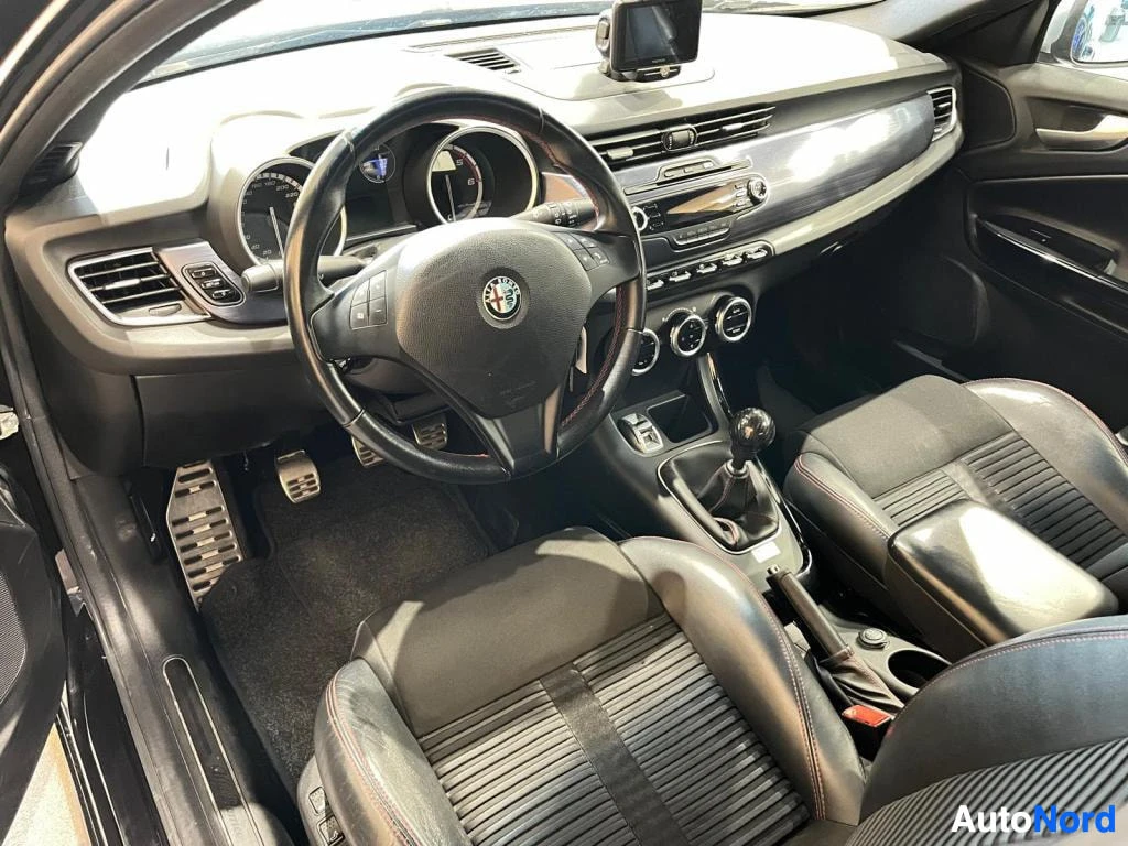 Muu: Ohjaamo kuljettajan puolelta ylhäältä: Alfa Romeo -logoinen rattion, manuaalivaihtoheitin, metallipolkimet, kosketusnäyttö ja mustat urheiluistuimet punaisilla