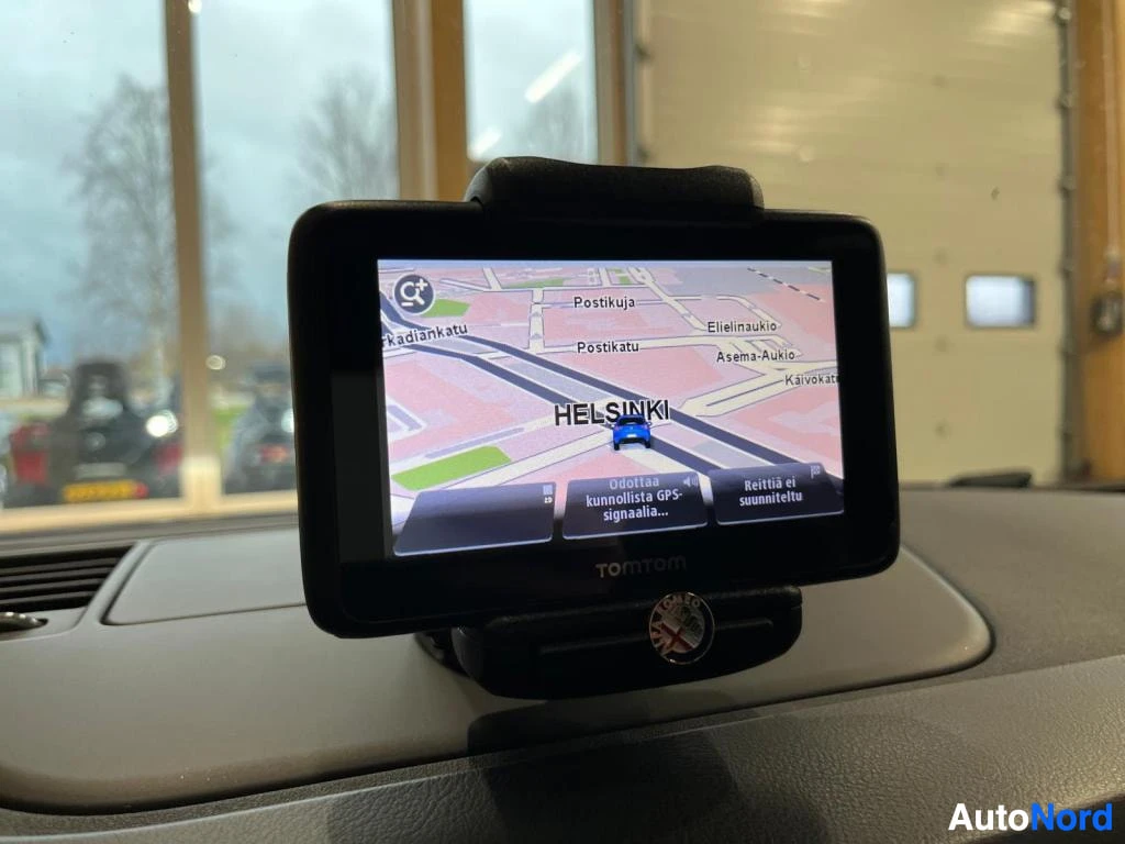 Muu: Kojelaudalla kiinnitetty TomTom-navigaattori näyttää Helsingin karttaa ja viestiä, että GPS-signaalia odotetaan.