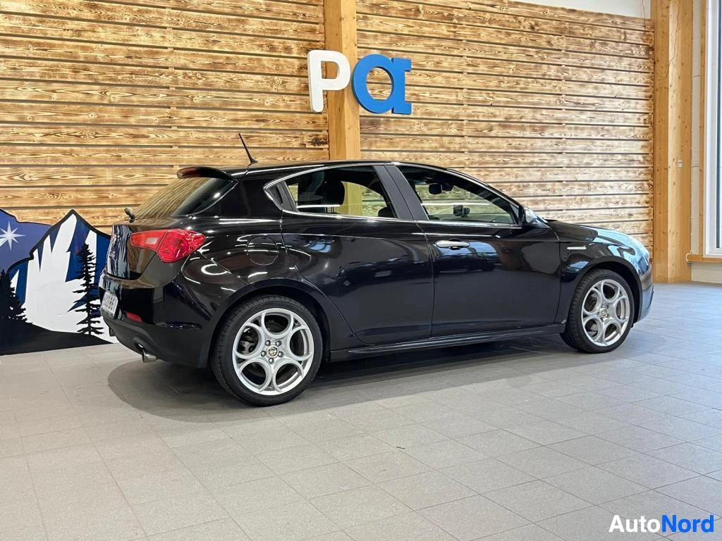 Takaviisto: Musta viistoperäinen henkilöauto takaa sivulta kuvattuna sisätiloissa.